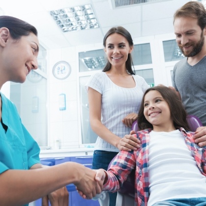 Dentist greeting young dental patient and her parents