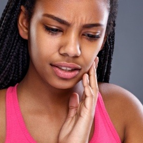 Woman with broken tooth holding cheek in pain