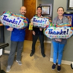 Three dental team members holding thanks balloons