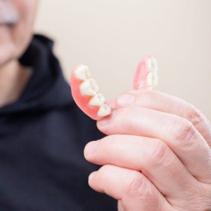 Hand holding a full denture to replace missing teeth