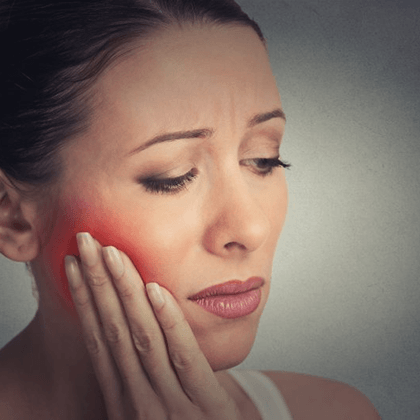 a woman holding her cheek due to tooth pain