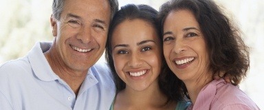 Family of three sharing healthy smiles after preventive dentistry