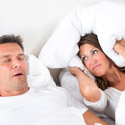 Woman covering her ears with pillow next to sleeping man