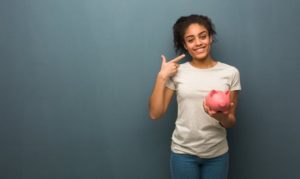 Woman holding a piggy bank and pointing towards her smile.